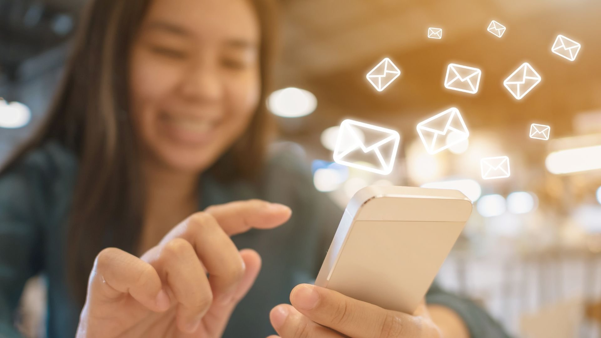 a person smiling at their phone while receiving email notifications from an email marketing agency which are surrounding the phone