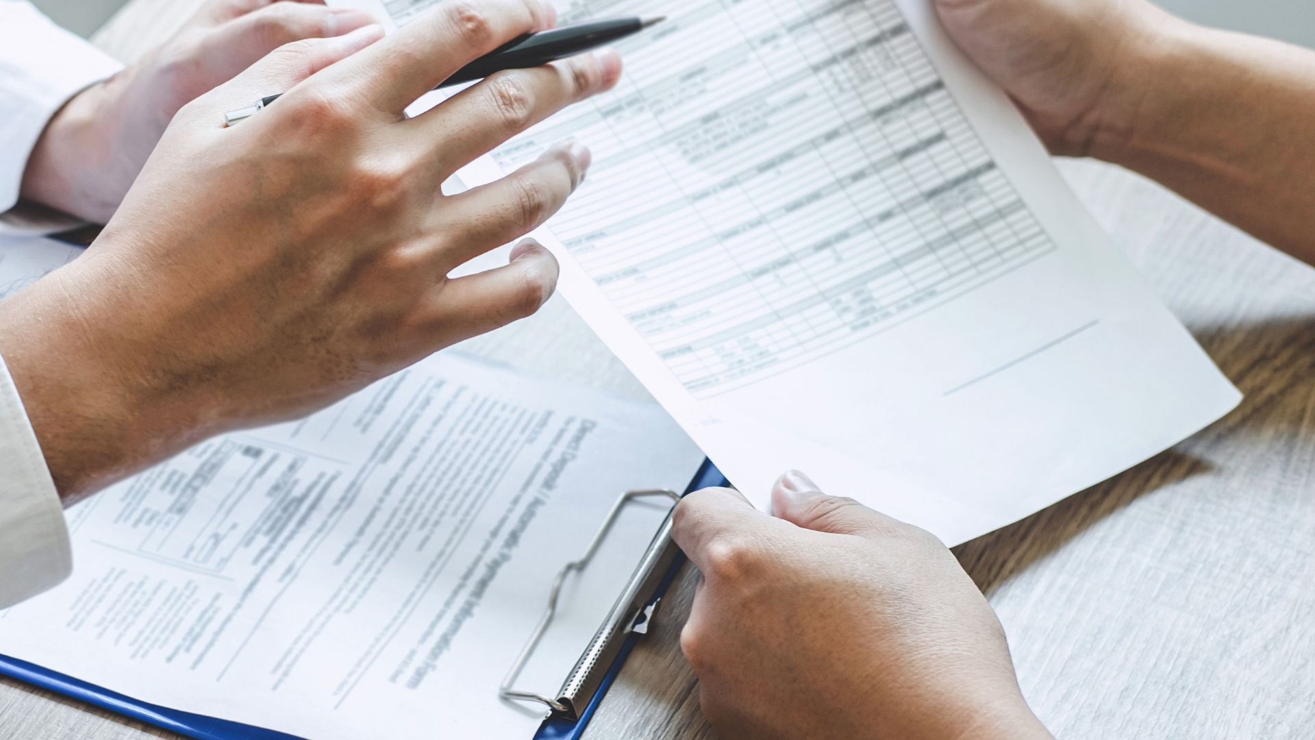 The hands of twooff-screen people are shown as they evaluate SEM digital marketing data on paper and a clip board. 