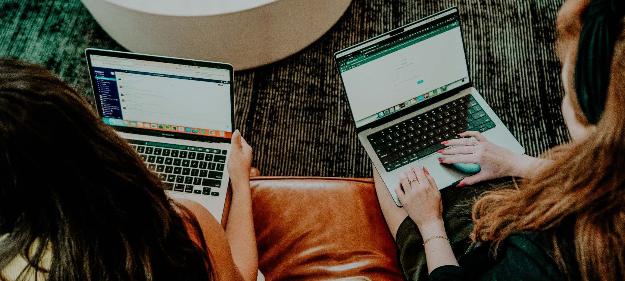 arial view of two people sitting on a leather couch with open laptops in their laps